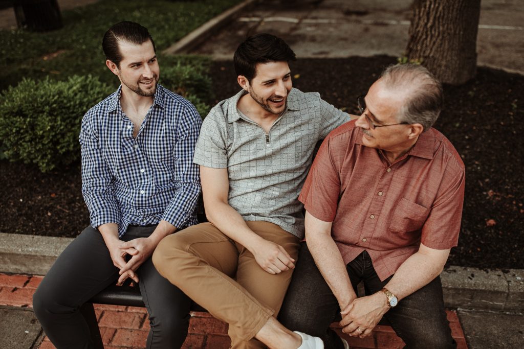 Three men sitting on a bench talking to each other.