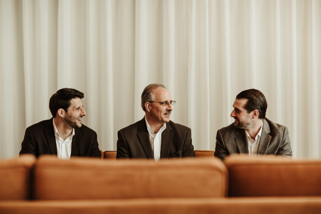 Three men sitting on a couch in front of a curtain.